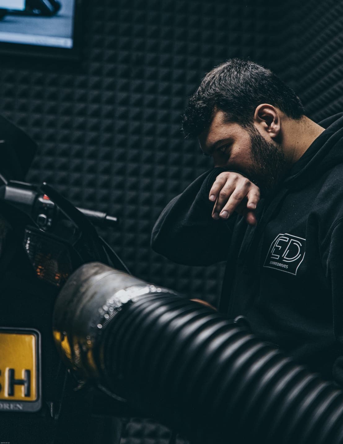 Emre in de studio naast een motor, in een EmreDrives-hoodie